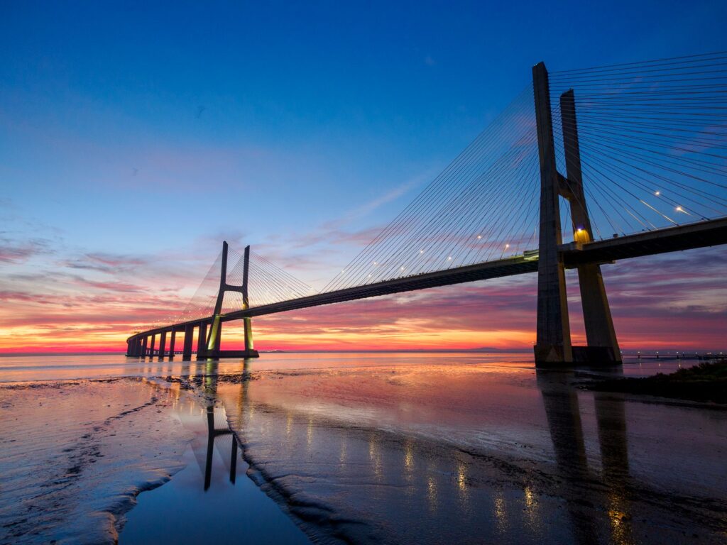 Stunning sunset over Vasco da Gama Bridge reflecting in the waters of Lisbon's coast.
