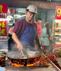 A street food vendor cooking at a vibrant night market in Penang, Malaysia.