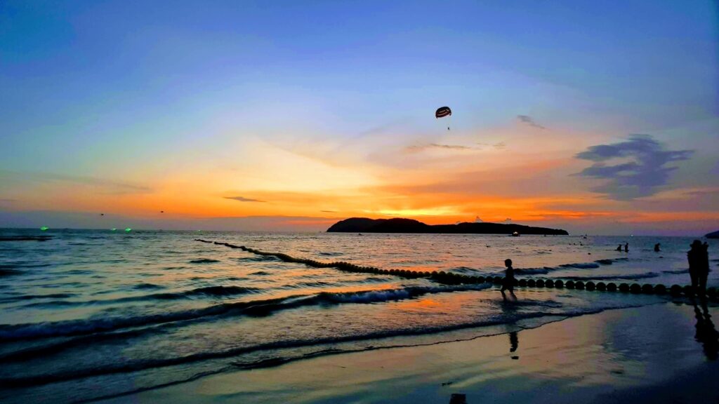 people in beach under orange sky at sunset
