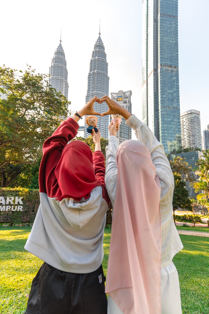 Two women form heart shape with hands, city skyline background