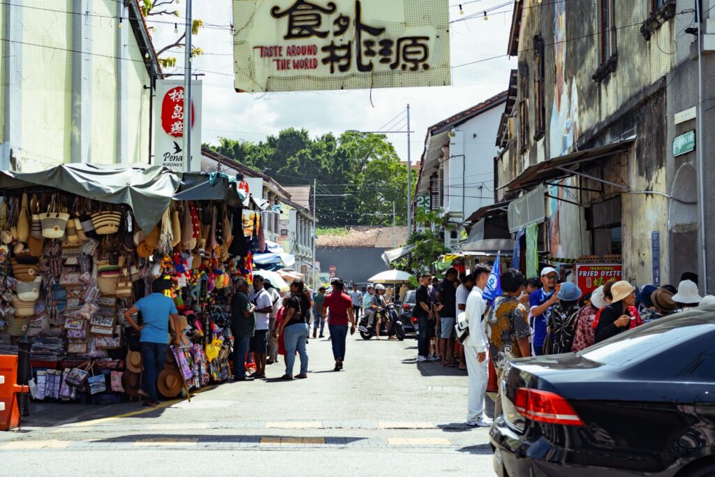 Colorful street market in George Town, Penang, bustling with locals and tourists under a bright sky.